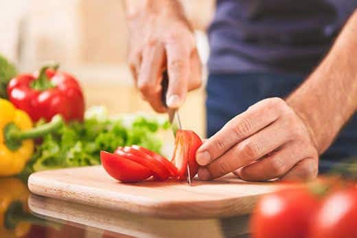 imagem de comida caseira - vista ampliada de uma mão masculina a cortar tomate sobre uma tábua de madeira em casa