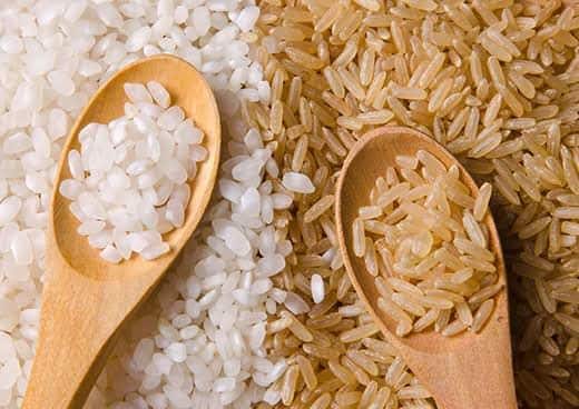 Arroz branco e integral com duas colheres de madeira em cima lado a lado com arroz.